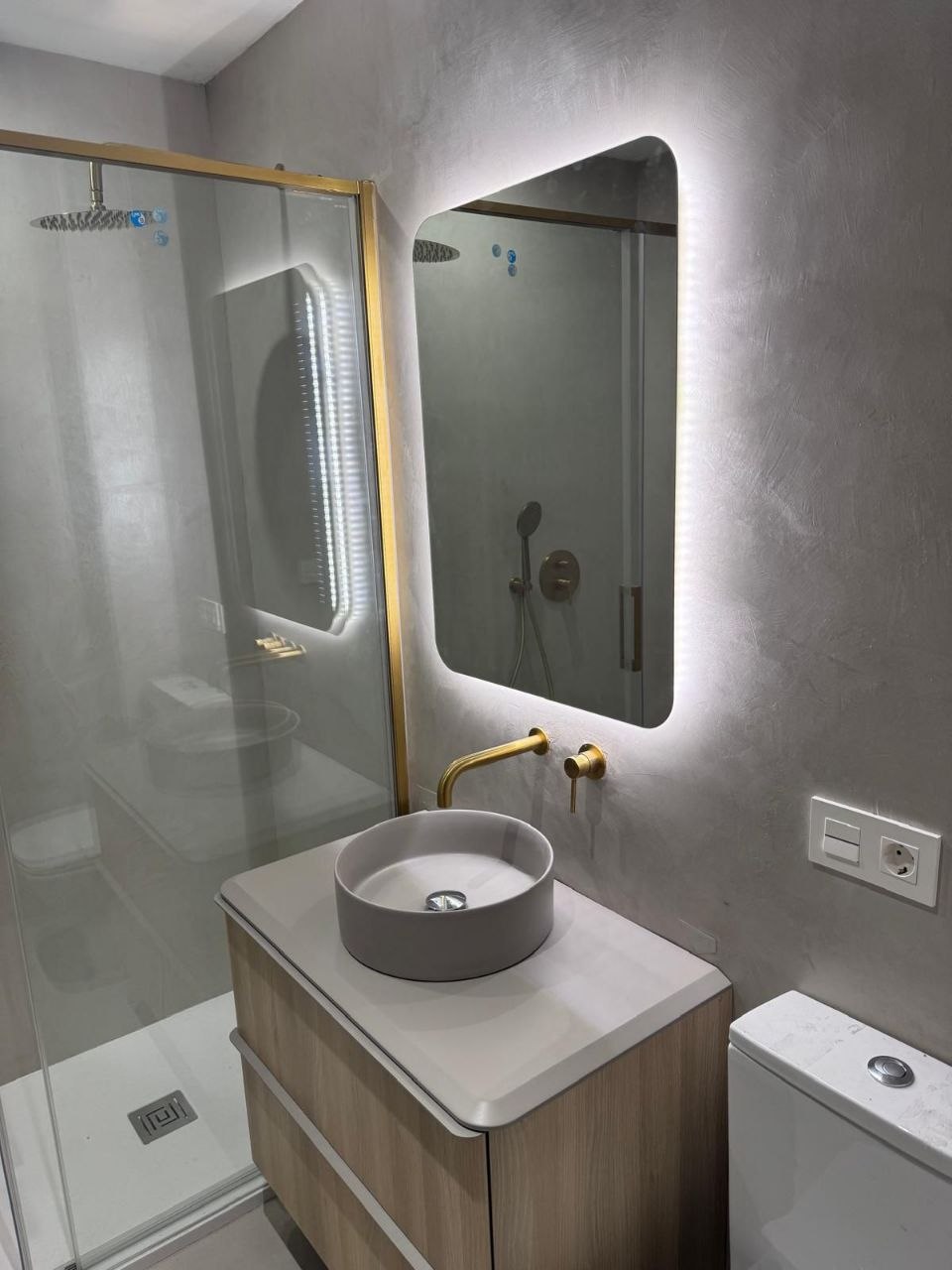 Grey microcement bathroom with brass fixtures and a backlit mirror